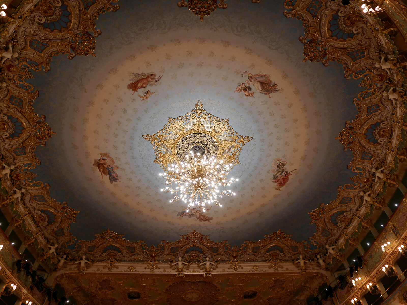 Teatro La Fenice : The ceiling features a large gilded chandelier at its center, surrounded by concentric circles in shades of blue that create the illusion of a dome, despite the ceiling being flat